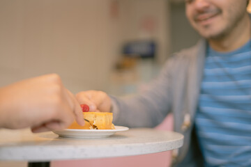 Couple sharing slice of cake with raspberry in coffee shop