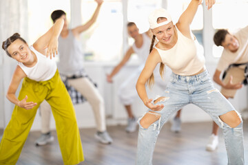 During rehearsal workout teen girl in baseball cap dances hip hop with friends. Team of dancers performs sequence of steps in combination with hand movements, energetic hobby leisure activity of youth