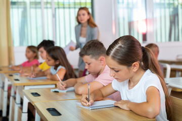Fototapeta premium Diligent elementary school student tween girl studying with classmates, making notes of teacher lecture