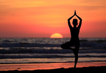 Woman practicing yoga on the beach at sunset