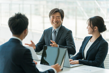 企業のオフィスで笑顔で会議・ミーティング・商談をするビジネスマン・ビジネスウーマン
