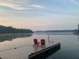 Two red adirondack chairs overlooking the bay at sunrise with the landscape reflected in the water