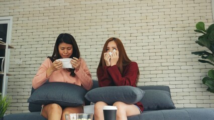 Two woman watch TV Series drama sadness crying on sofa couch home living room. Girl best friends sharing life problems together sad unhappy. displeased emotion sitting talking together at home