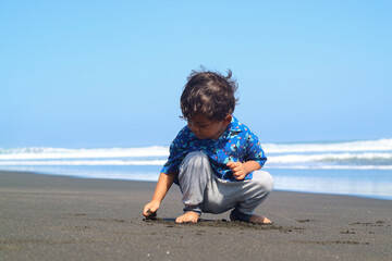 Happy fun Asian child cute little boy playing sand with toy sand tools at a tropical sea beach in holiday summer on sunset time, tourist trip concept