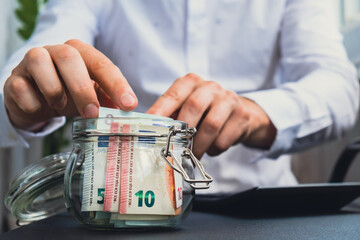 Man hands counting expenses banknotes of euro cash from glass jar in the piggy bank on calculator....
