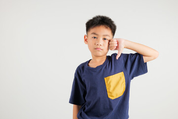 Portrait disheartened Asian young kid boy displaying a thumbs down gesture, symbolizing dislike. Studio shot isolated on white with ample copy space, primary child portraying negative and sad look