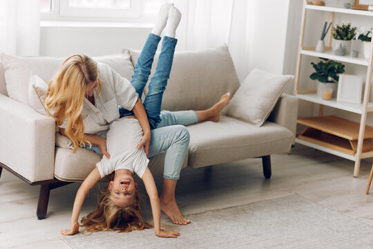 Mother and daughter bonding time doing handstands on the living room couch in a playful, cozy home setting