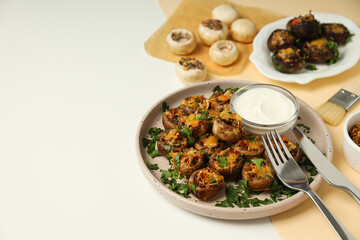 Stuffed mushrooms on plates, sauce and cutlery on white background, space for text