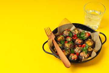 Stuffed mushrooms in frying pan and glass of water on yellow background, space for text