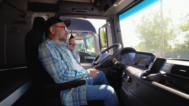 Senior truck driver sitting in cab speaks on the radio walkie talkie