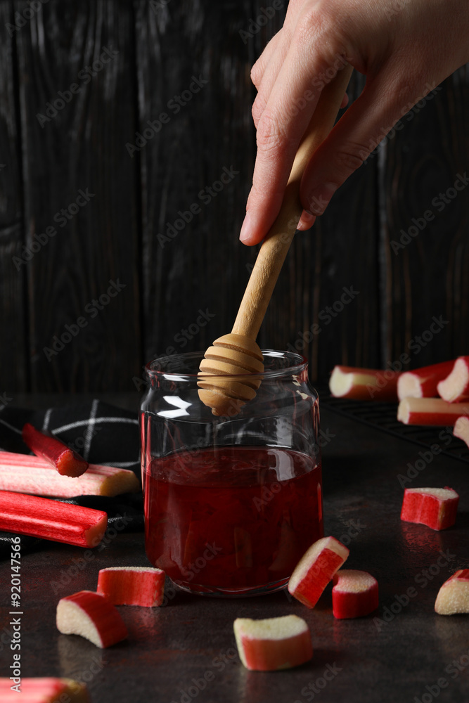 Sticker Rhubarb jelly in a jar with fresh rhubarb stems on a dark background