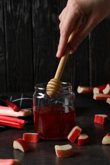 Rhubarb jelly in a jar with fresh rhubarb stems on a dark background