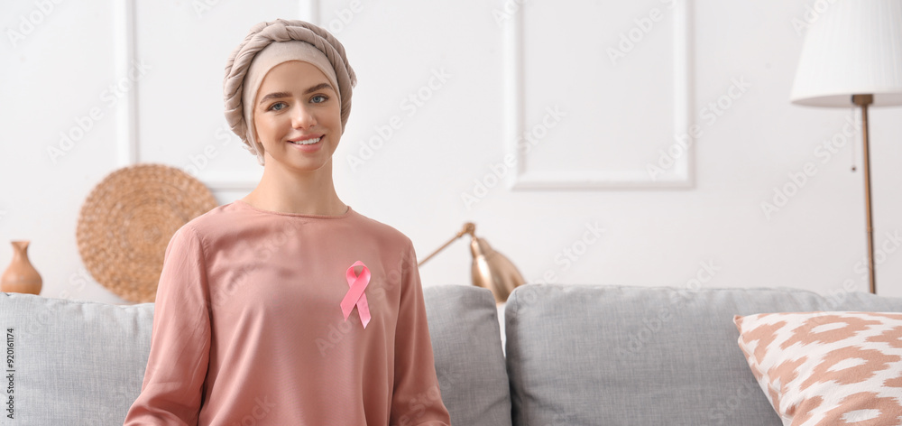 Wall mural young woman after chemotherapy with ribbon at home. breast cancer awareness concept