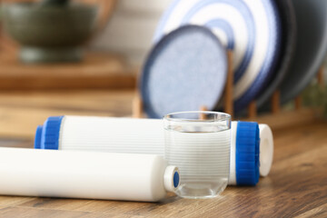 Glass of water with filters on wooden table in kitchen