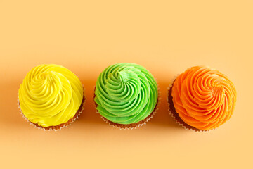 Tasty colorful cupcakes on orange background