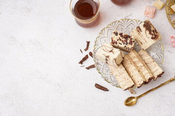 Pieces of tasty marble halva and glass with Turkish tea on white background