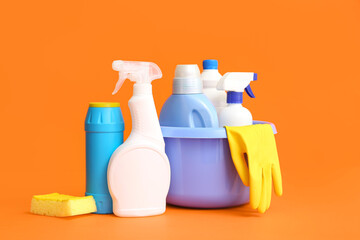 Bowl with different cleaning supplies on orange background