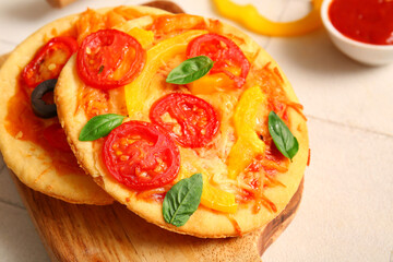 Board with different tasty mini pizzas on white tile background