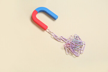 Magnet attracting paper clips on beige background
