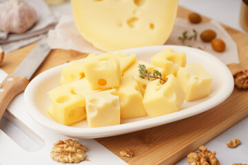 Board and plate with pieces of Swiss cheese on white table
