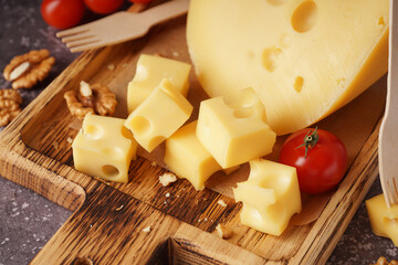 Board with pieces of Swiss cheese and tomatoes on grey background