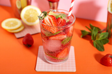 Glass of fresh strawberry mojito with straw and ingredients on orange table near pink wall