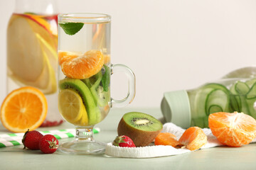 Glass and bottles of infused water with different sliced fruits on grey table