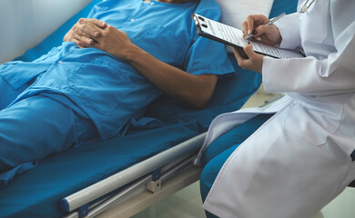 Hospitalized man lying in bed while doctor checking his pulse. Female physician examining male patient in hospital room.