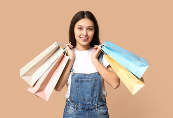 Fashionable young Asian woman in stylish denim overalls with shopping bags on brown background