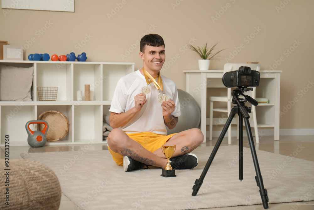 Canvas Prints Sporty happy male blogger with gold cup and medals recording video at home