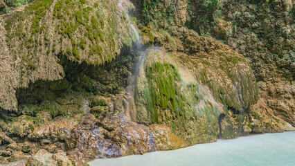 An exotic tropical waterfall. Thin streams of water flow down the mossy openwork ledges of the rock, forming a veil. Turquoise lake at the foot. Philippines. Cebu. Tumalog Falls