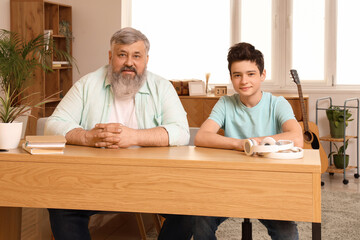 Happy grandfather with his cute grandson sitting at table in room