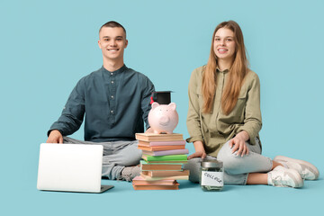 Young students sitting with piggy bank, books and laptop on blue background. Concept of savings for...