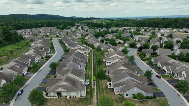 Suburban neighborhood with rows of houses and green lawns in America. Streets lined with neatly arranged homes. Aerial reverse dolly in summer.