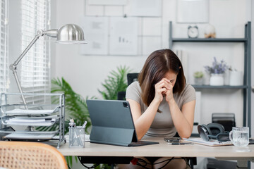 A businesswoman sitting at her desk with her head in her hands, showing stress and frustration in a modern office setting.