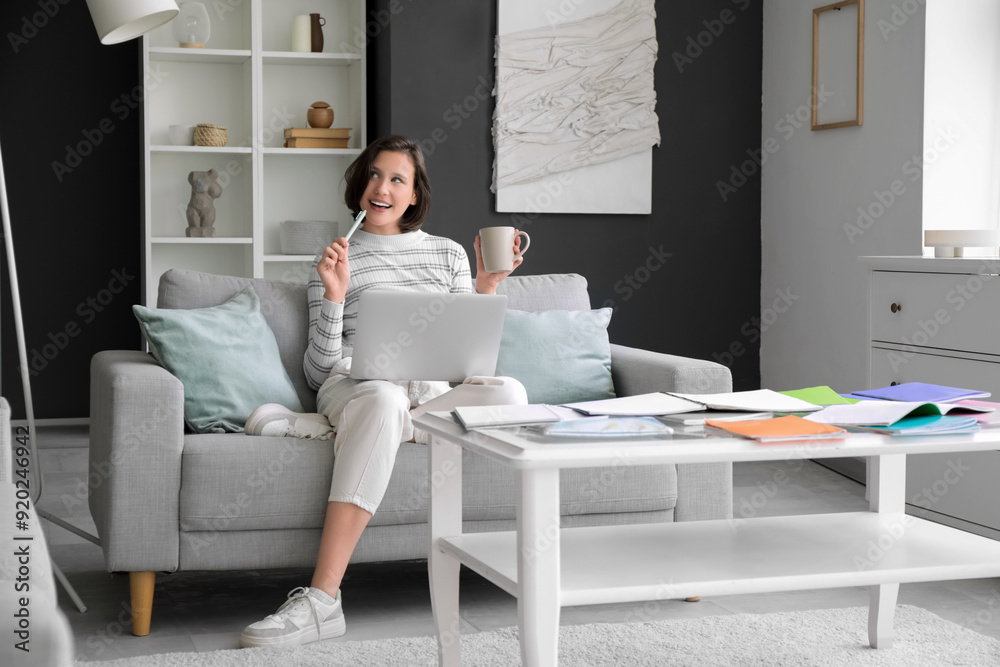 Poster Thoughtful female student with cup and laptop studying on sofa at home