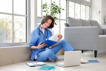 Female medical intern with clipboard studying near window in clinic