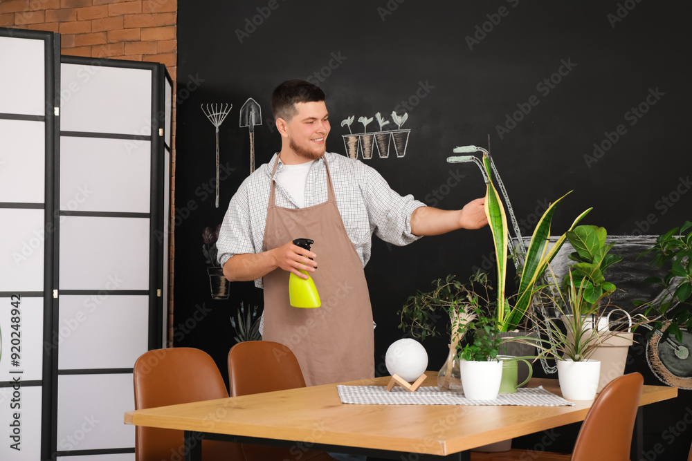 Poster Young male gardener spraying plant in room