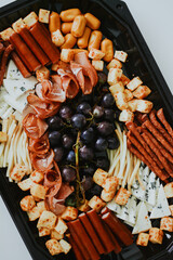 macro shooting of various snacks in the form of meats and cheeses with grape on a black plate 