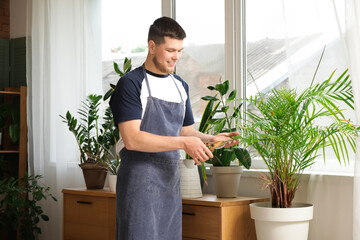 Young male gardener pruning plants in room