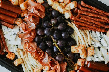 macro shooting of various snacks in the form of meats and cheeses with grape on a black plate 