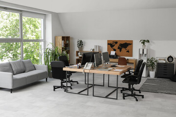 Interior of stylish office with grey sofa, workplaces, computers and armchairs