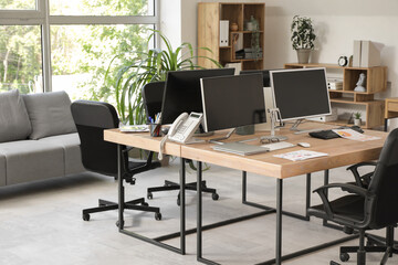 Interior of stylish office with grey sofa, workplaces, computers and armchairs
