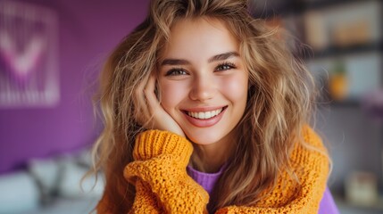 Smiling woman with blonde hair in a cozy orange sweater, posing against a purple background indoors.