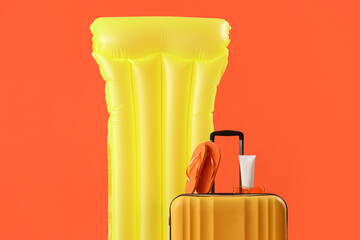 Inflatable mattress and suitcase on orange background. Travel concept