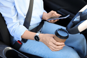 Fastened female driver with coffee cup sitting in car, closeup