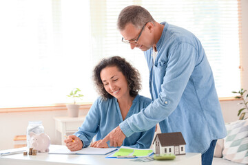 Happy couple with piggy bank and money jar doing calculation at home
