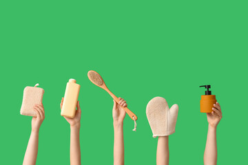 Female hands with bottles of cosmetic products, bath sponge and massage brush on green background