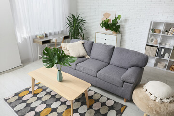 Modern interior of living room with tropical monstera leaves in vase on table and stylish sofa