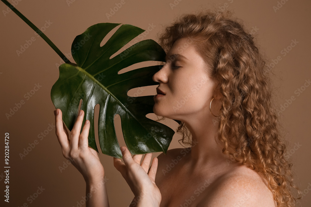 Wall mural beautiful young woman with tropical monstera leaf on brown background